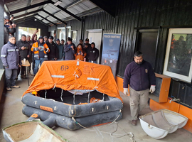 En un galpón, en tierra firme, un instructor enseña a un grupo de tripulantes de embarcaciones mercantes cómo armar un bote salvavidas.